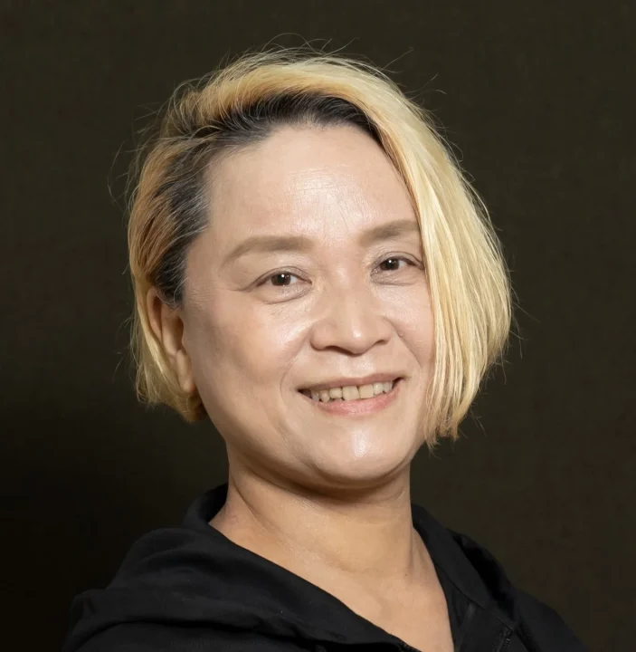 短い金髪の女性が黒いパーカーを着用し微笑んでいるポートレート写真