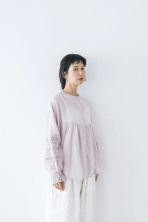 淡いピンクのレース袖ブラウスと白いスカートを着用し、ナチュラルでフェミニンな雰囲気のショートヘアの女性