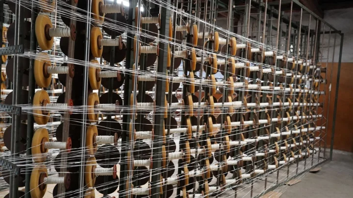 白い糸が巻かれたボビンが並ぶ産業機械