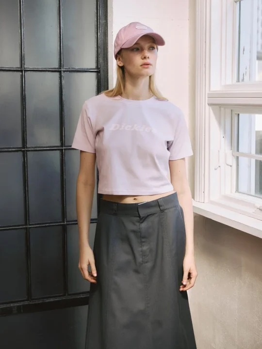 ピンクのクロップTシャツとキャップ、ロングスカートを着用した女性