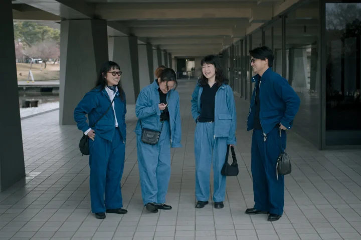 青いコーデュロイの服を着た4人の男女が談笑する集合写真