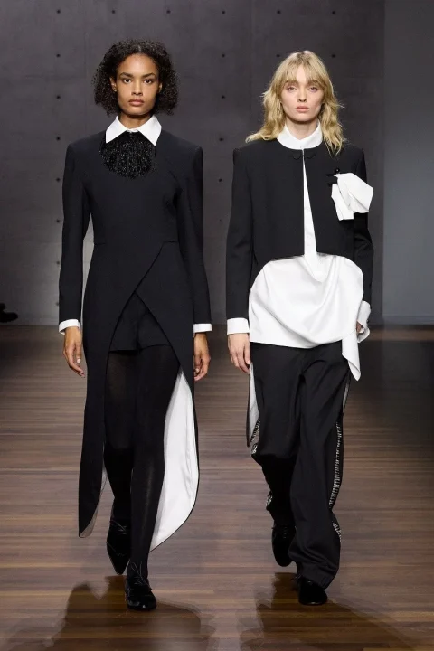 黒のロングジャケットと白い襟、黒のショートジャケットと白いシャツ、黒のパンツを着用した2人の女性モデル