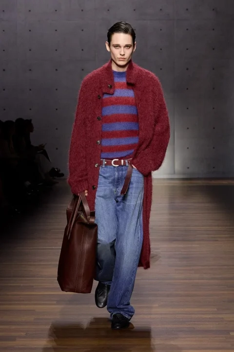ダークレッドの毛羽立ったロングコート、赤と青のストライプセーター、ルーズなジーンズを着用したモデル