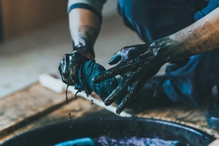 濃い染料に染まった手が布を絞る様子