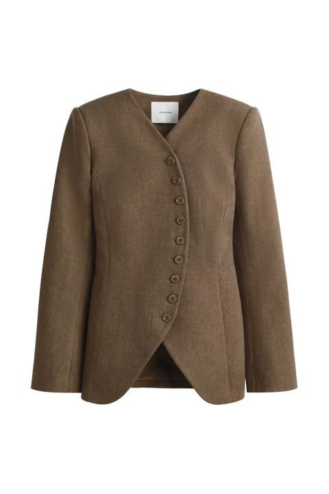白背景に置かれたブラウンのノーカラージャケット。Vネックで、斜めに配置された複数のボタンが特徴