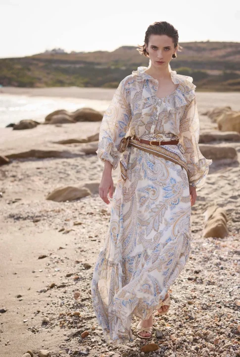女性モデルがペイズリー柄のマキシドレスを着用し、砂浜に立つ様子