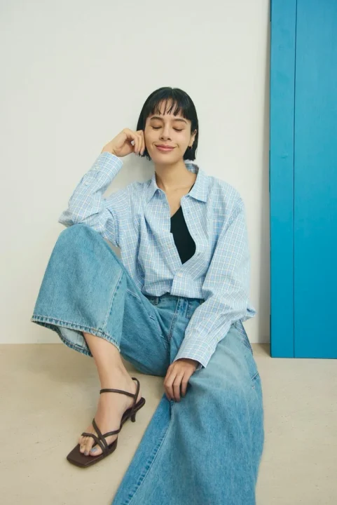 床に座るチェックシャツとワイドデニムパンツ