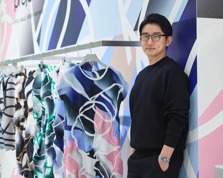 鮮やかなプリーツ素材の服が並ぶラックの横に立つ男性