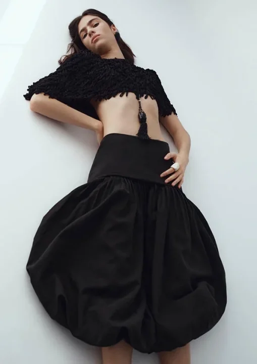 黒いクロップ丈のトップスとボリュームのあるバルーンスカートを着用し、シックなファッションスタイルを表現する女性