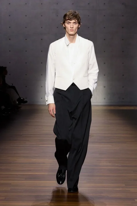 白いシャツとベストに、黒いワイドパンツとエナメルシューズを合わせた男性モデル