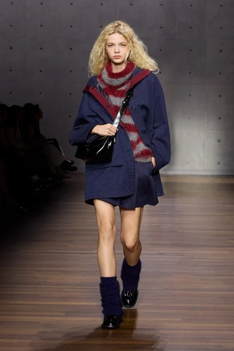 ネイビーのショートコートとショートパンツ、赤とグレーのボーダースカーフを着用した金髪のモデル