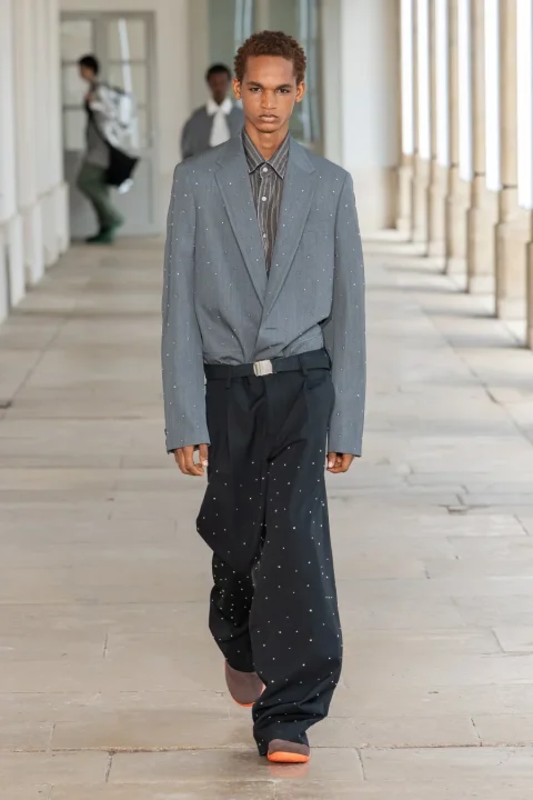 スタッズがあしらわれたグレーのブレザーと黒のワイドパンツを着用した男性モデル