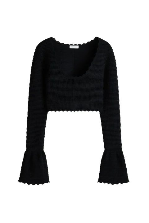 白い背景に置かれた、黒いクロップド丈のニットセーター。スカラップネックと裾、そしてベルスリーブが特徴