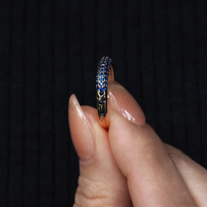 青い宝石が埋め込まれたゴールドの指輪を持つ指