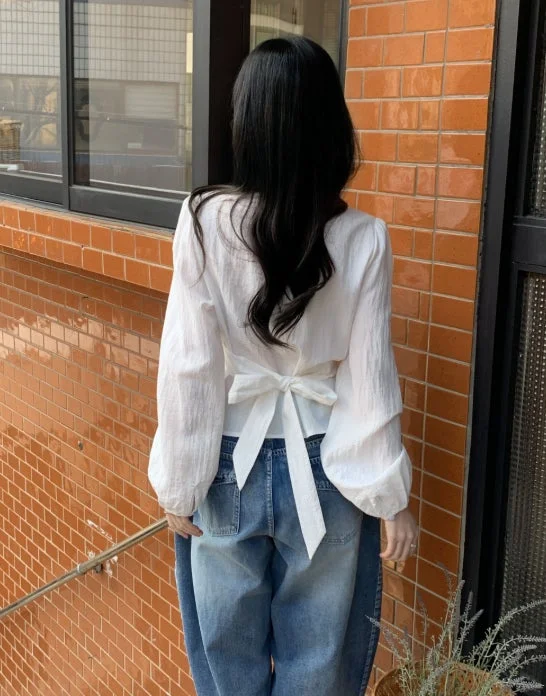 白いリボン付きブラウスとゆったりとしたデニムパンツを着用した女性の後ろ姿