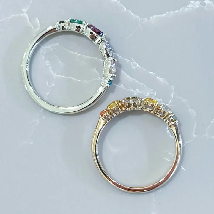 大理石調の背景に、様々な色の宝石が並んだ二つのエタニティリングが写っています。