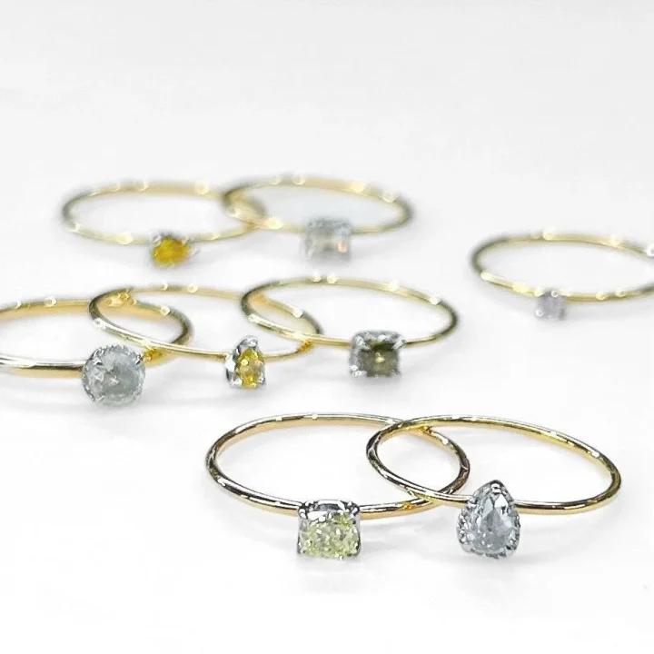 白い背景に、様々な色とカットの天然ダイヤモンドがあしらわれた華奢なゴールドリングが複数並べられています。