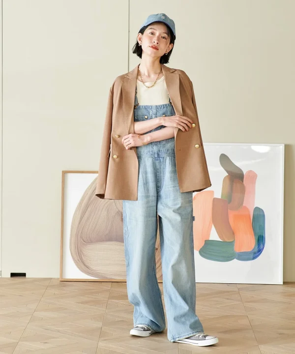 デニムのオーバーオールにブラウンのブレザーを羽織った女性