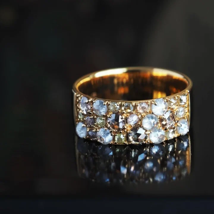 暗い背景に置かれた、様々な色合いの小さな宝石がちりばめられた美しいゴールドリングのクローズアップ画像です。