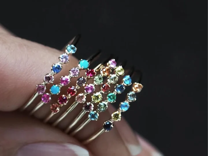 複数の細いゴールドリングが指に重ねられ、それぞれに様々な色の小さな宝石が連なっている様子が写っています。