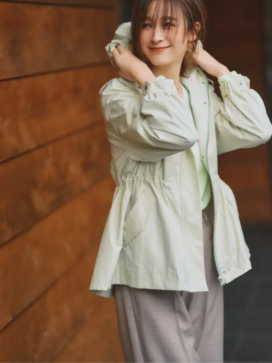 淡いグリーンのフード付きジャケットを着用した藤井サチさんの笑顔のポートレート