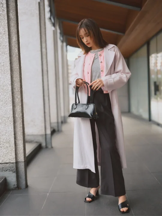 ピンクのトレンチコートと黒のワイドパンツを合わせた藤井サチさんの全身ショット