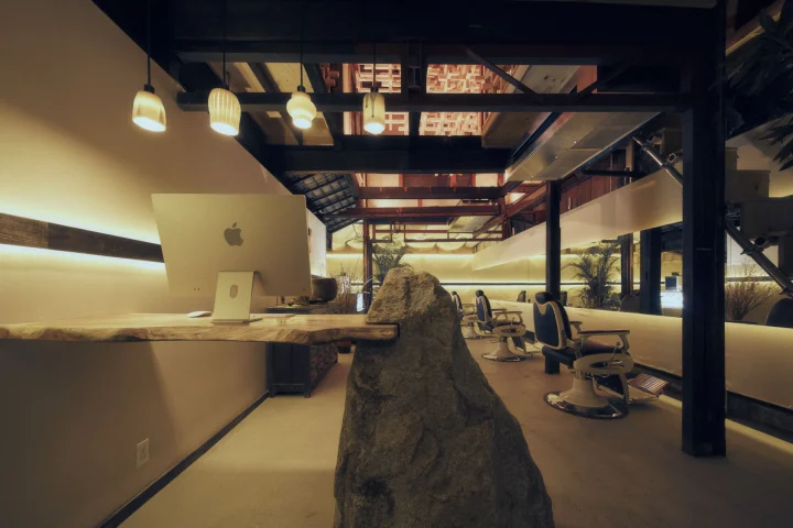 天然石と木材を組み合わせたモダンな理髪店または美容室の店内。Apple iMacが置かれた受付と、奥には理容椅子が見えます。和の要素を取り入れた洗練された空間デザインが特徴です。