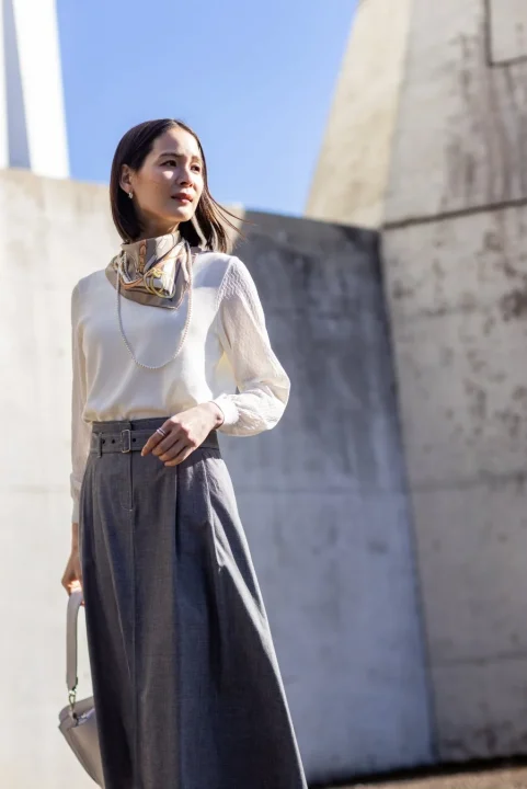 白いブラウスとグレーのロングスカート、スカーフを着用した女性