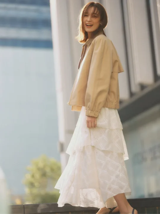 ベージュのジャケットと白いティアードレーススカートを着用した藤井サチさんの全身ショット