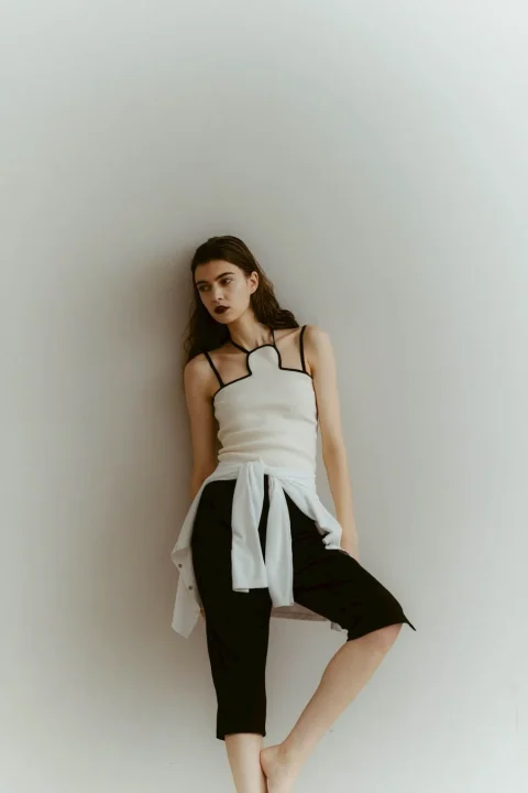 白いトップスと黒いクロップドパンツを着用し、白いシャツを腰に巻いたカジュアルでスタイリッシュな装いの女性