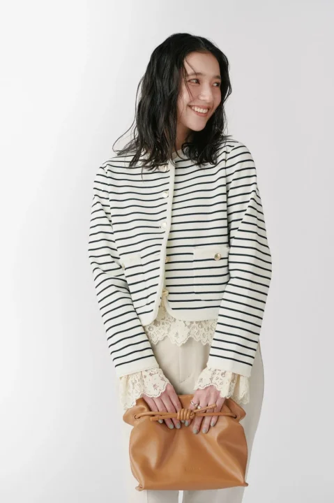 ゴールドボタンニットジャケットを着用し微笑むモデル