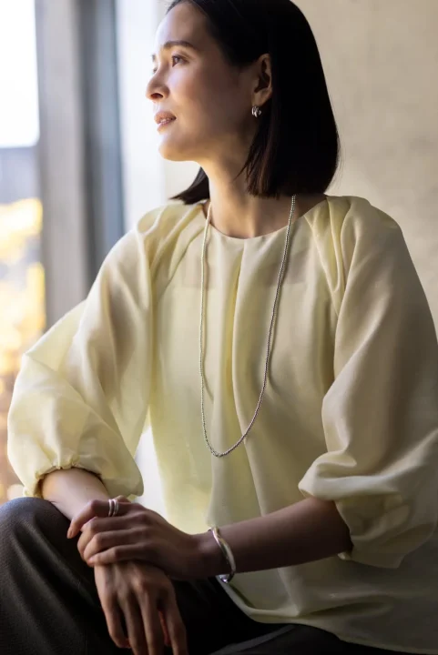 淡い黄色のブラウスを着用し、窓辺に座る女性