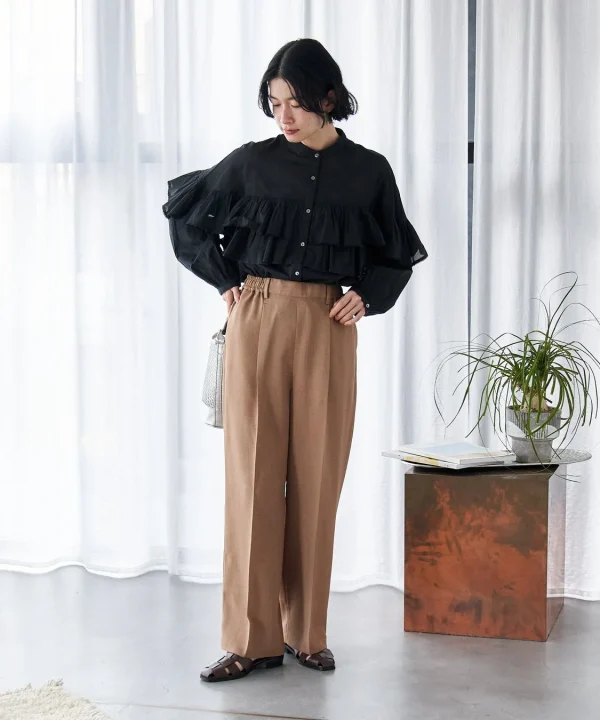 黒のフリルブラウスと茶色のワイドパンツを着用した女性