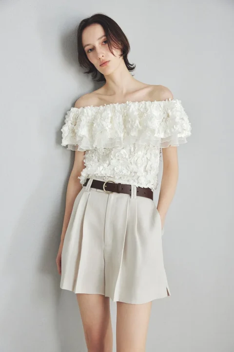 白い花柄のオフショルダートップスとベージュのショートパンツ