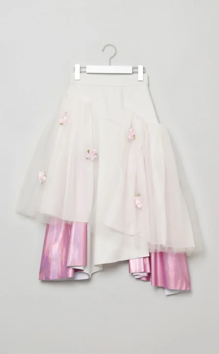 白いチュールと光沢のあるピンクの生地が特徴的な、バラの装飾が施されたアシンメトリーなデザインのスカート