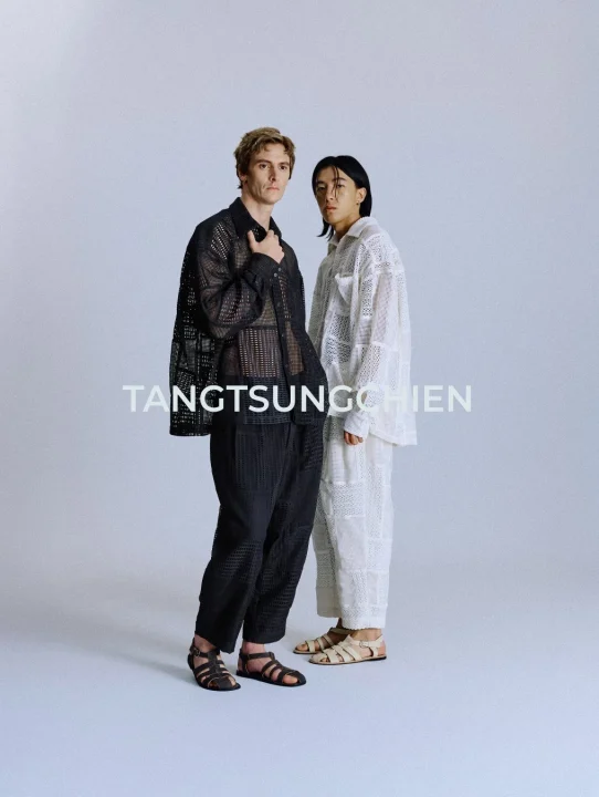 淡いグレーの背景で、メッシュ素材の服を着用した2人のモデルがポーズをとっています。一人は黒い服とサンダルを、もう一人は白い服とサンダルを身につけており、モダンなファッションスタイルを表現しています。