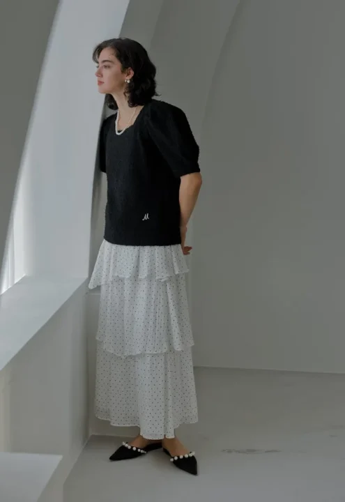 白ティアードのドット柄スカートと黒パフスリーブトップスを着た女性