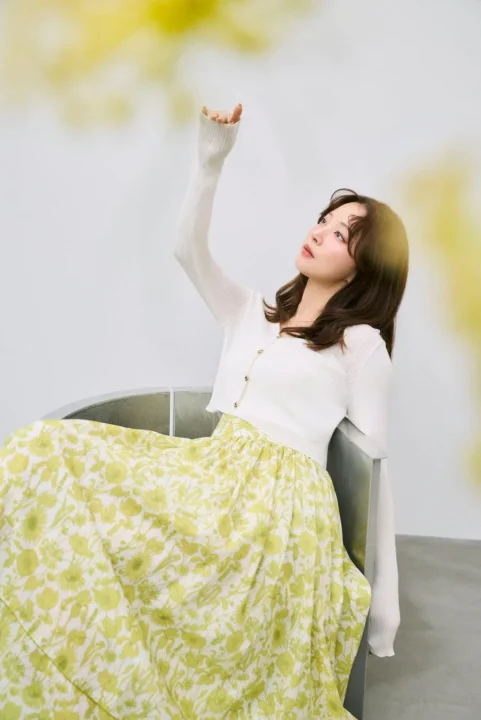 白いカーディガンと緑の花柄ロングスカート、座っている