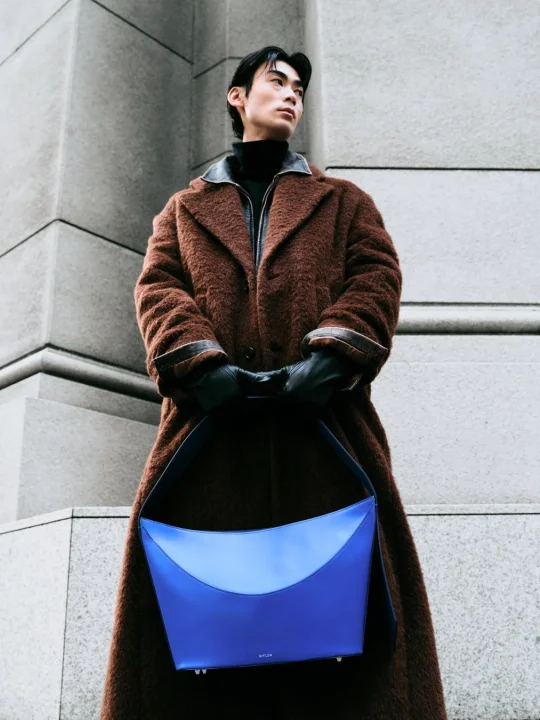 茶色のコートと青いバッグを持った男性