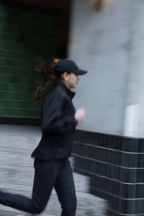 黒いキャップとトレーニングウェアを着用した人物が走っている様子を捉えた画像です。動きによるブレがあり、疾走感が表現されています。