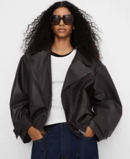 黒いジャケットとサングラスを着用し、長い巻き髪の女性がポーズ