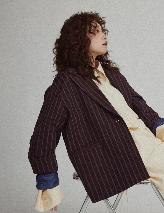 ストライプ柄のジャケットと黄色のシャツを着用し、横を向いて座っている女性