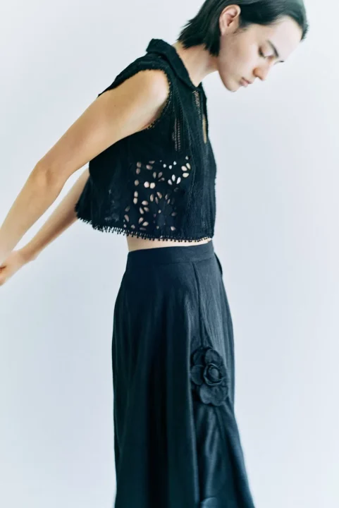 黒いノースリーブのクロップトップと花の装飾が付いたロングスカートを着用した人物