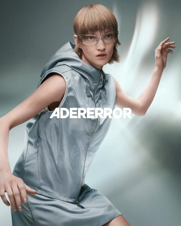 ADERERRORのモデルがクリアなメガネとグレーのノースリーブフーディを着用している画像