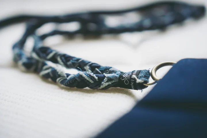 白い布地の上に置かれた、青と白の編み込みストラップと金属リングのクローズアップ写真。ストラップには「Stony Point Recycle」と書かれたタグが見えます。
