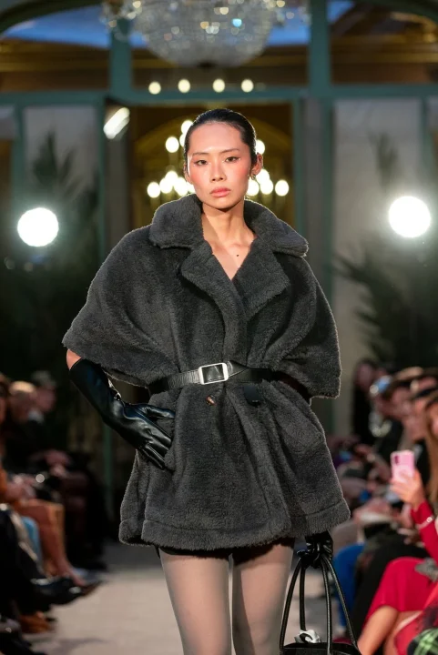 チャコールグレーのテディコートに黒いベルトとレザーグローブ、黒いハンドバッグを合わせ、透け感のあるタイツを着用したモデル