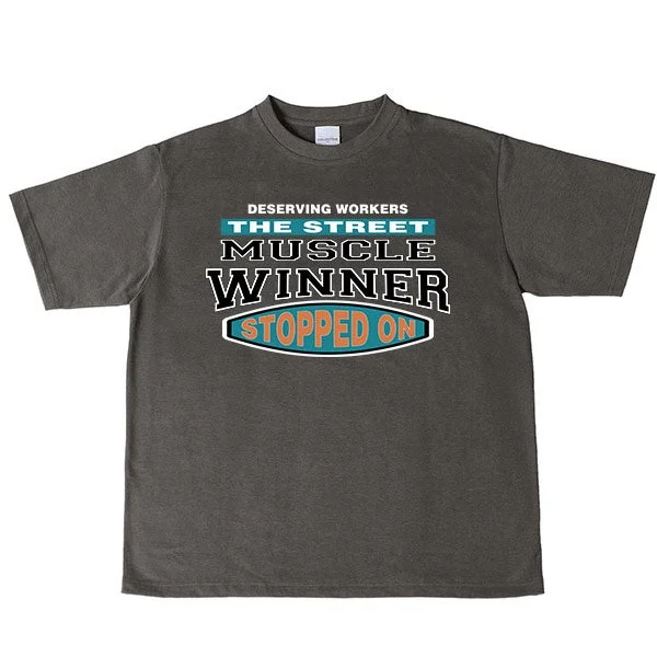 ダークグレーのTシャツに、レトロなフォントで「DESERVING WORKERS THE STREET MUSCLE WINNER STOPPED ON」という英語のメッセージがプリントされています。