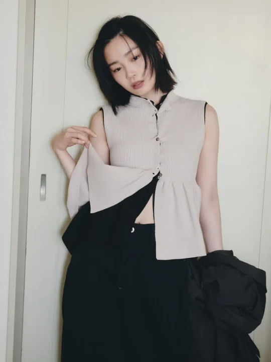 ショートヘアの女性がノースリーブのベージュのリブトップスと黒いパンツを着用