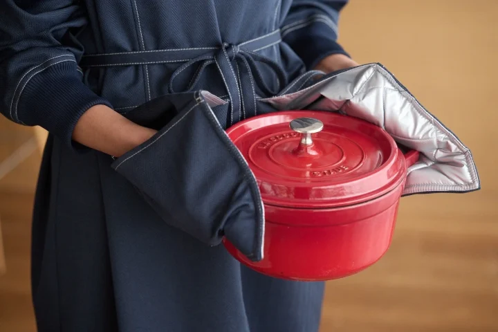 ネイビーの割烹着を着用し、ストウブ鍋を持つ手元