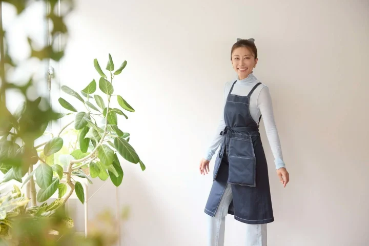 ネイビーのエプロンを着用し、観葉植物のそばに立つ女性